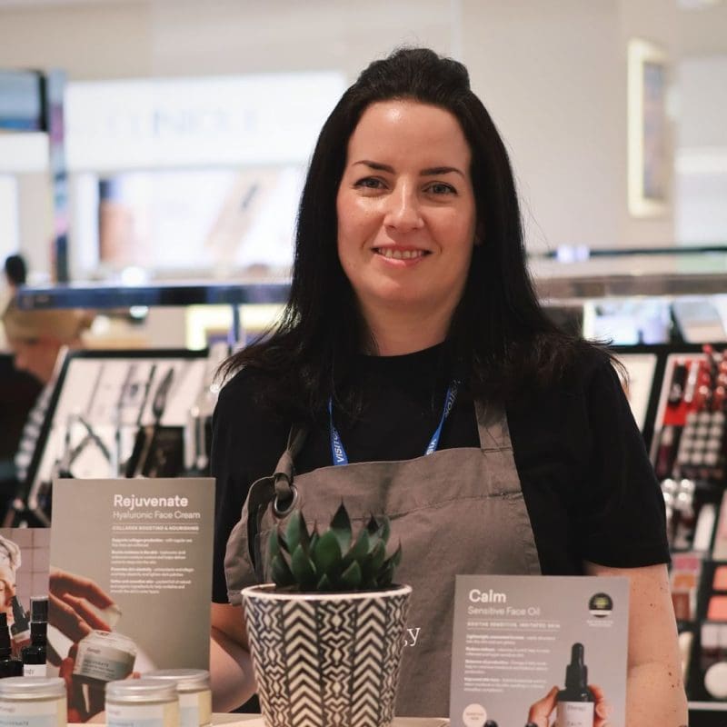 Louisa Tidy student successful story at ray cochrane academy (woman standing behind a skincare stand)